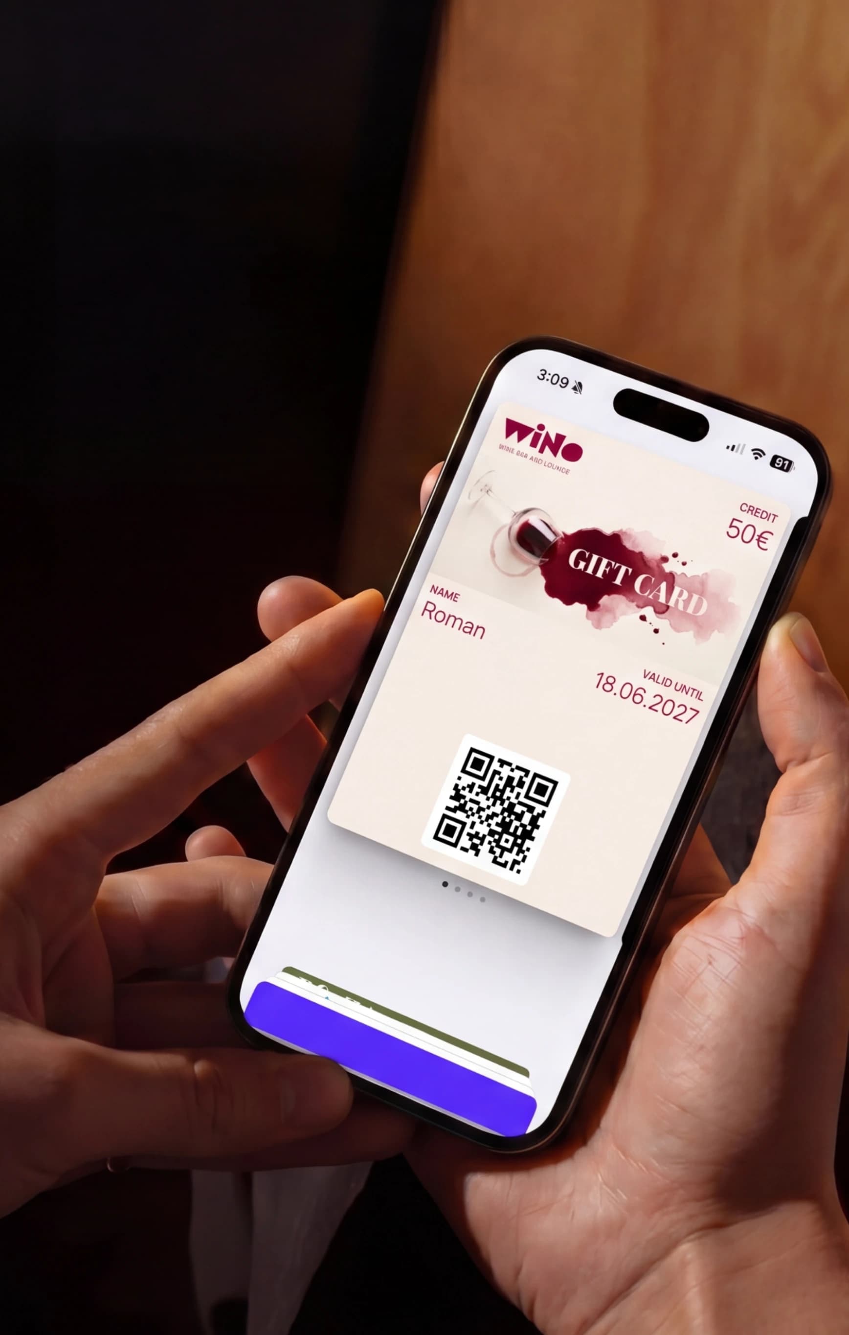 Hands holding a phone with a branded gift card open in the wallet, showing the credit and a QR code