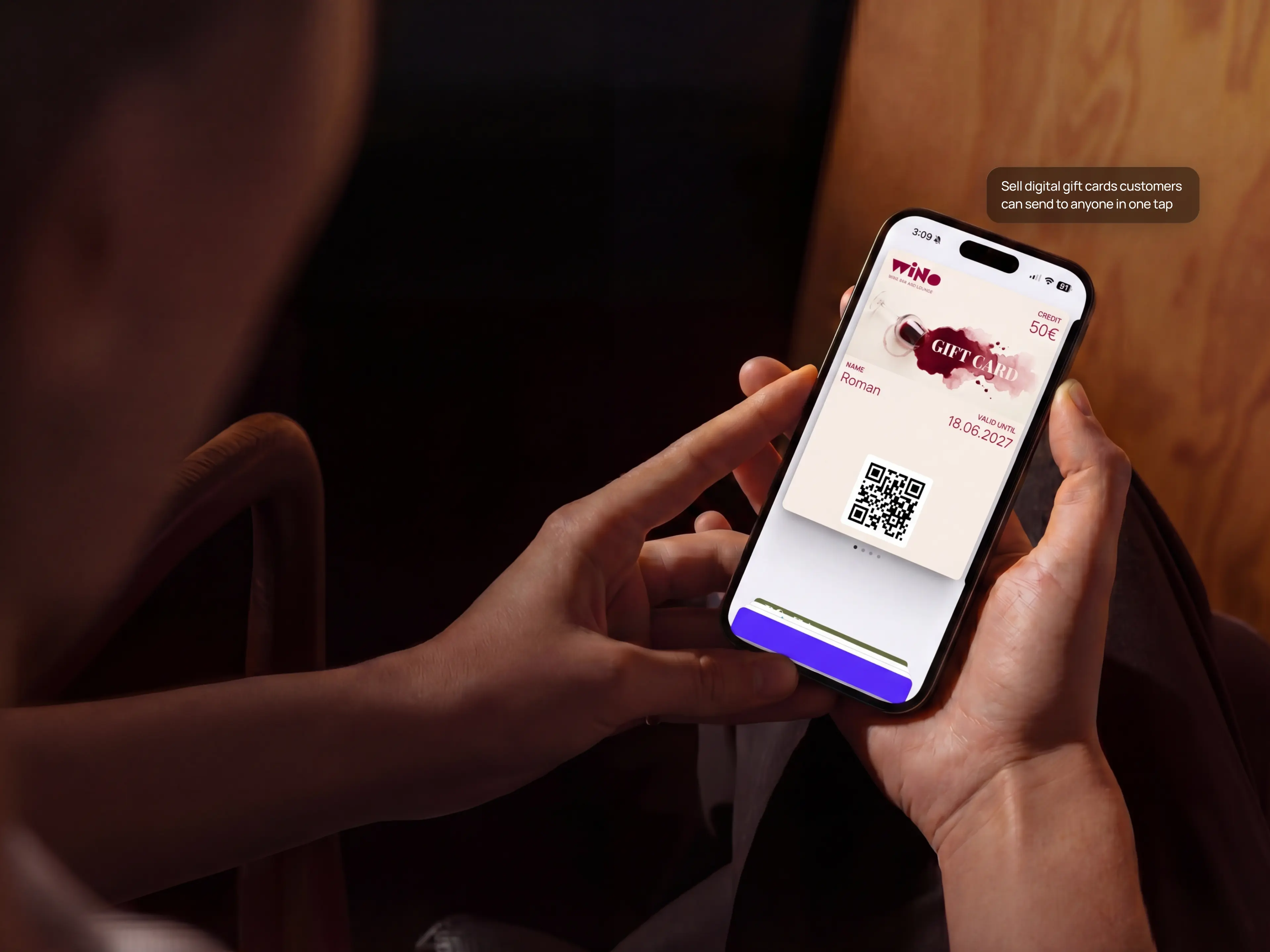 Hands holding a phone with a branded gift card open in the wallet, showing the credit and a QR code